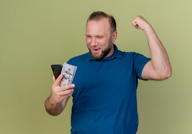 Joyeux homme slave adulte tenant un dollar et un téléphone mobile en les regardant et en faisant oui geste