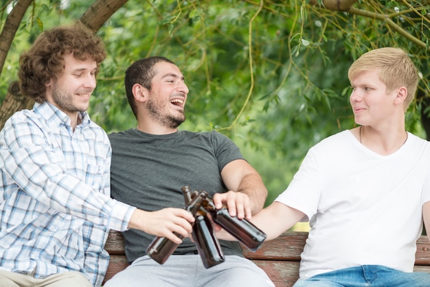 Photo gratuite joyeux hommes buvant de la bière sur le banc