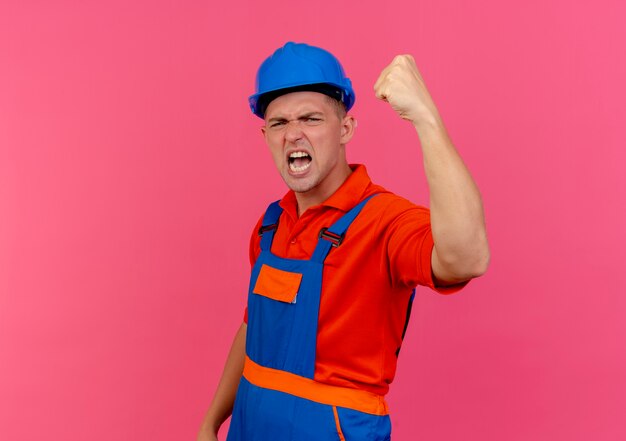 Photo gratuite joyeux jeune constructeur masculin portant l'uniforme et un casque de sécurité faisant un geste fort