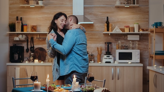 Joyeux jeune couple dansant et s'embrassant lors d'un dîner romantique. Heureux couple amoureux dînant ensemble à la maison, savourant le repas, célébrant leur anniversaire.