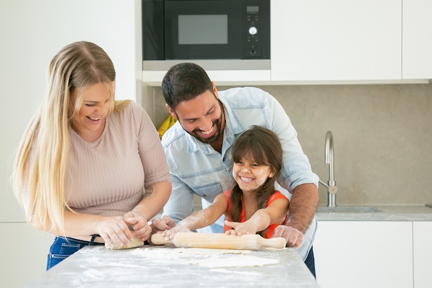 Joyeux jeune couple et fille avec de la poudre de fleur sur le visage en riant pendant la cuisson ensemble.