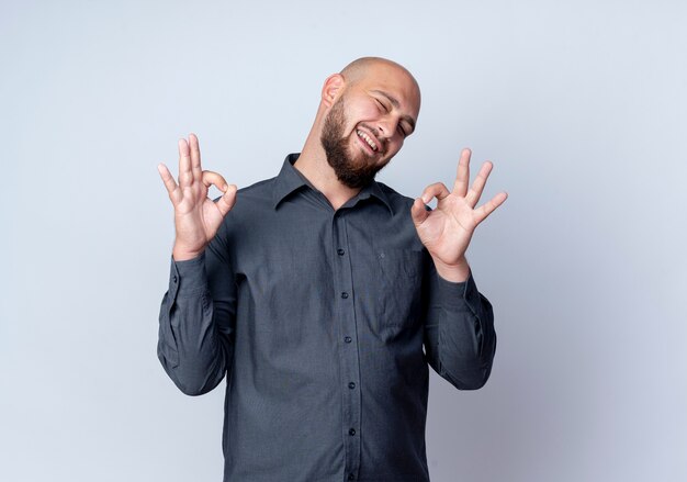 Joyeux jeune homme de centre d'appels chauve clignant des yeux et faisant des signes ok isolés sur blanc