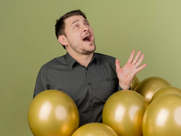 Joyeux jeune homme de fête vêtu d'une chemise noire debout derrière des ballons isolés sur vert olive