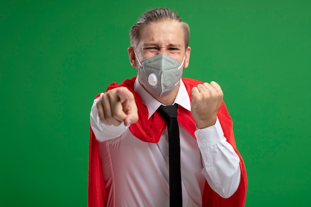 Joyeux jeune homme de super-héros portant un masque médical et une cravate vous montrant le geste isolé sur fond vert