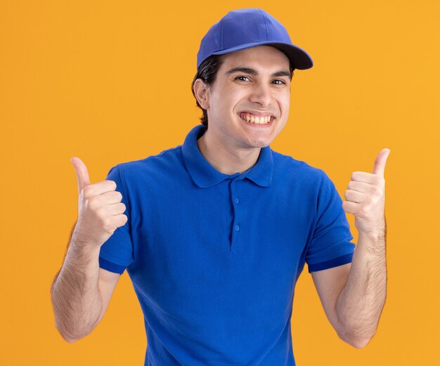 Joyeux jeune livreur caucasien en uniforme bleu et casquette montrant les pouces vers le haut