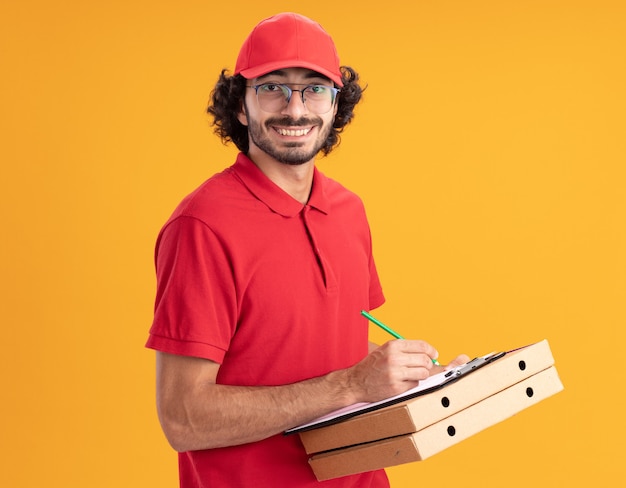 Joyeux jeune livreur caucasien en uniforme rouge et casquette portant des lunettes