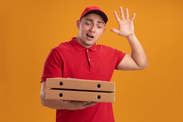 Joyeux jeune livreur en uniforme avec capuchon tenant des boîtes de pizza montrant bonjour geste isolé sur mur orange
