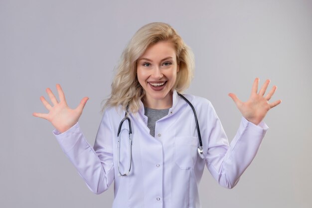 Joyeux jeune médecin portant un stéthoscope en robe médicale se propage les mains sur le mur blanc