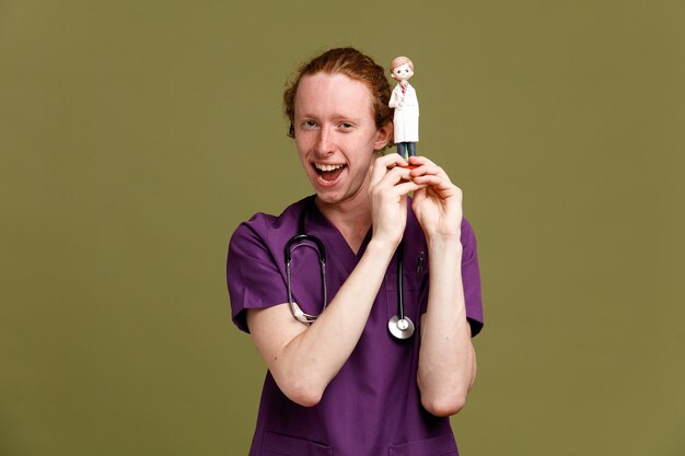 Joyeux jeune médecin de sexe masculin en uniforme avec stéthoscope tenant un jouet isolé sur fond vert