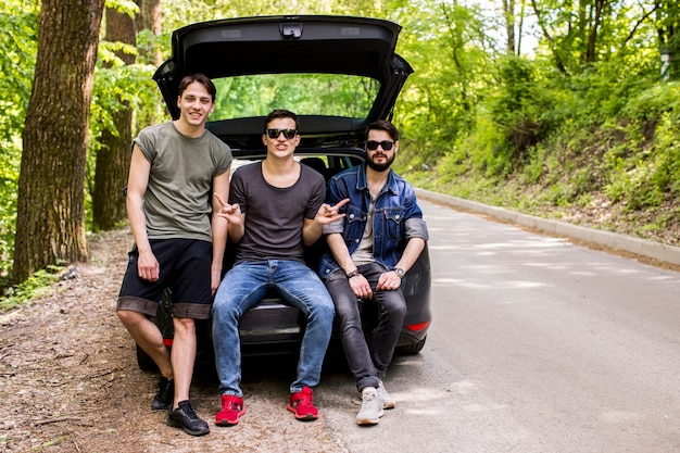 Joyeux jeunes mecs assis dans le coffre sur la route forestière