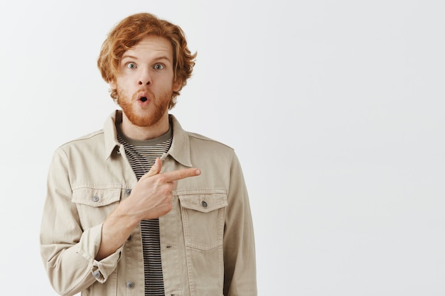 Joyeux mec rousse barbu posant contre le mur blanc