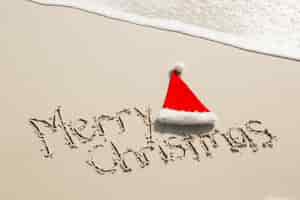 Photo gratuite joyeux noël écrit sur le sable avec le chapeau de santa