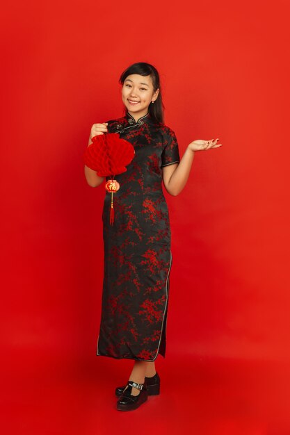 Joyeux nouvel an chinois 2020. Portrait de jeune fille asiatique isolé sur fond rouge. Le modèle féminin en vêtements traditionnels a l'air heureux et souriant avec une décoration. Célébration, vacances, émotions.