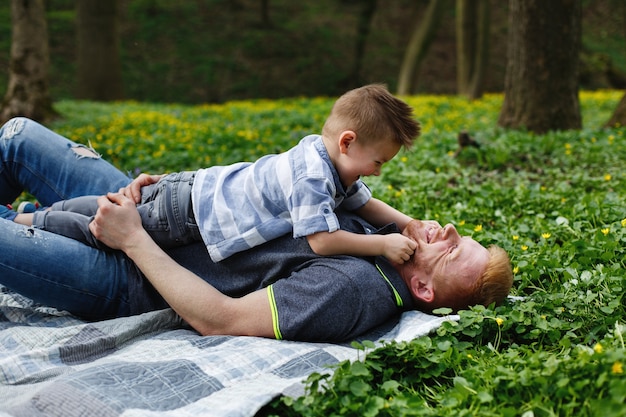 Joyeux papa et fils s&#39;amuser à jouer sur le plaid dans un parc verdoyant