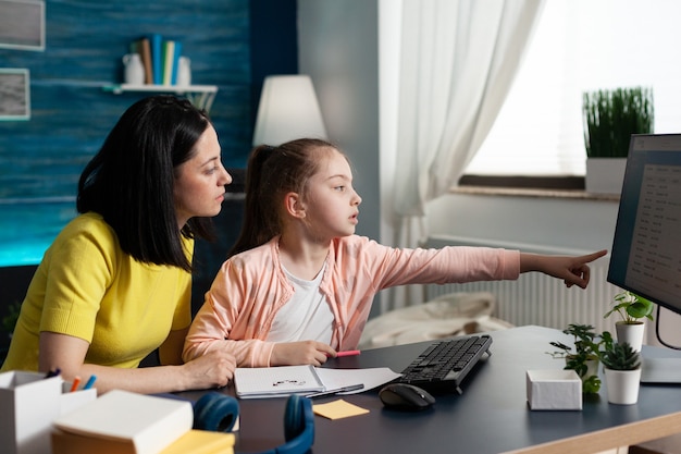 Joyeux parent assis à côté de sa fille faisant ses devoirs scolaires ensemble