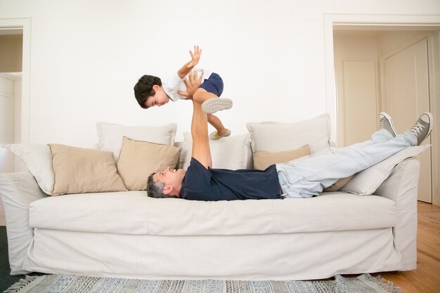 Joyeux père allongé sur le canapé et tenant son fils.