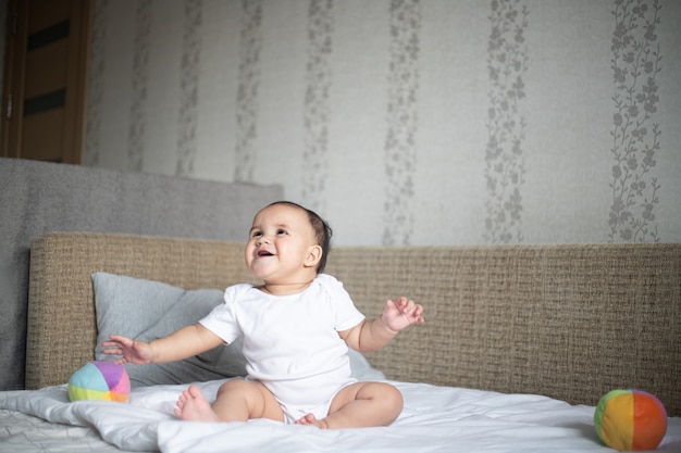 Joyeux petit bébé jouant sur un lit contre un mur sous les lumières dans une pièce