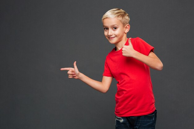 Joyeux petit garçon enfant pointant montrant les pouces vers le haut.