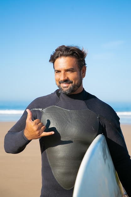 Joyeux surfeur barbu debout avec planche de surf et souriant