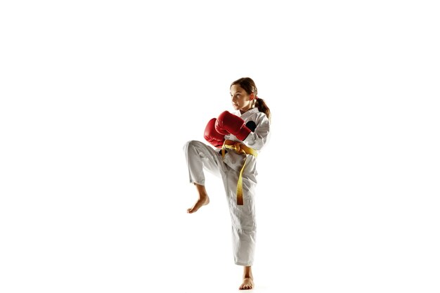 Junior confiant en kimono pratiquant le combat au corps à corps, les arts martiaux. Jeune combattante avec entraînement de ceinture jaune sur mur blanc. Concept de mode de vie sain, sport, action.