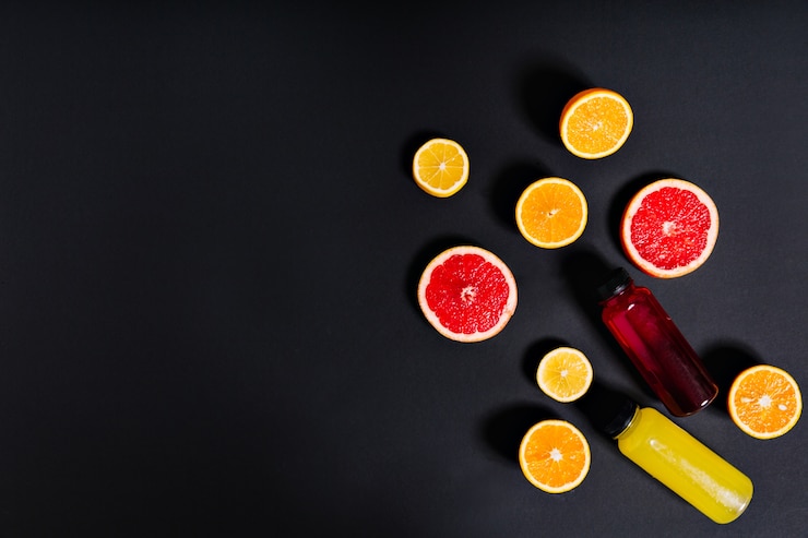 Photo gratuit jus d'agrumes fraîchement pressé dans des bouteilles se trouve entouré de moitiés d'orange, de citron et de pamplemousse sur le mur