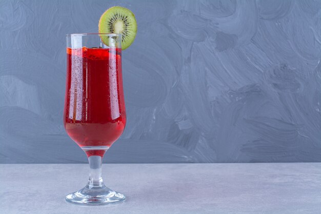 Jus de cerise dans un verre avec une tranche de kiwi sur une table en marbre.