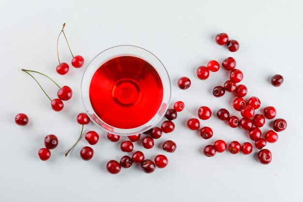 Jus de cerise dans un verre avec vue de dessus de cerises sur fond blanc