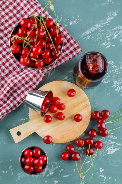 Photo gratuite jus de cerises, planche à découper dans une cruche sur plâtre et torchon, vue de dessus.