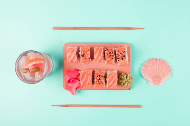 Jus de coquille Saint-Jacques et jus de pamplemousse avec sushi au saumon servis avec wasabi et gingembre mariné sur une planche à découper sur fond de menthe