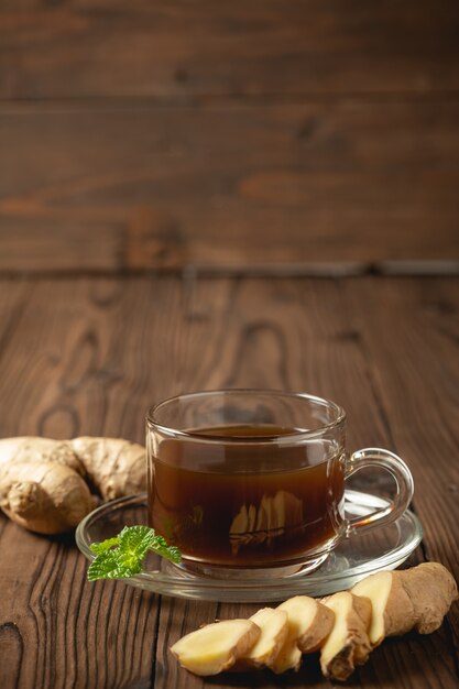 Jus de gingembre chaud et gingembre tranchés sur une table en bois.