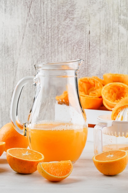 Jus d'orange avec des oranges, presse-agrumes dans une cruche sur une surface blanche