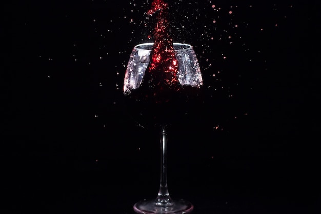 Le jus rouge éclabousse dans un verre de cristal debout dans un espace noir