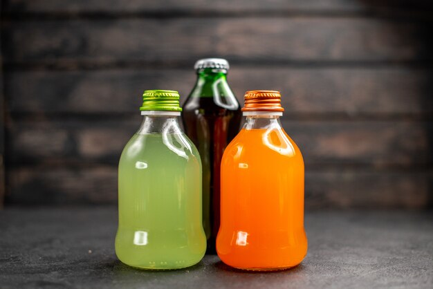 Jus de vue de face de différentes couleurs dans des bouteilles sur une surface en bois sombre