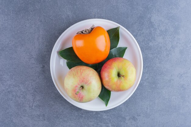 Kaki et pommes sur plaque sur la surface sombre