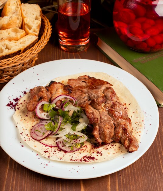 Kebab de bœuf, agneau, tranches d&#39;oignon, légumes et herbes, lavash dans une assiette blanche.