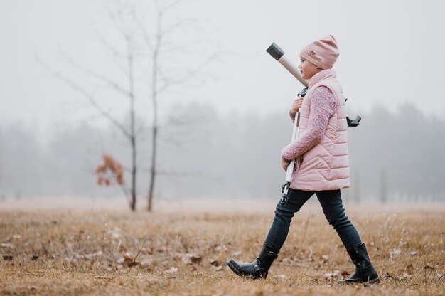 Photo gratuite kid sur le côté tenant un télescope à l'extérieur