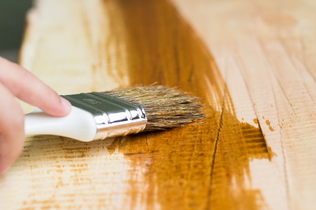 Kid Hand Varnishing une étagère en bois à l&#39;aide d&#39;un pinceau