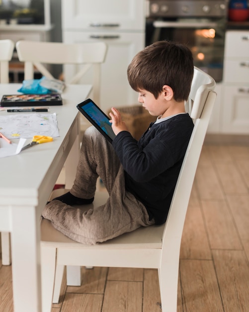 Photo gratuite kid plein tir sur chaise avec tablette