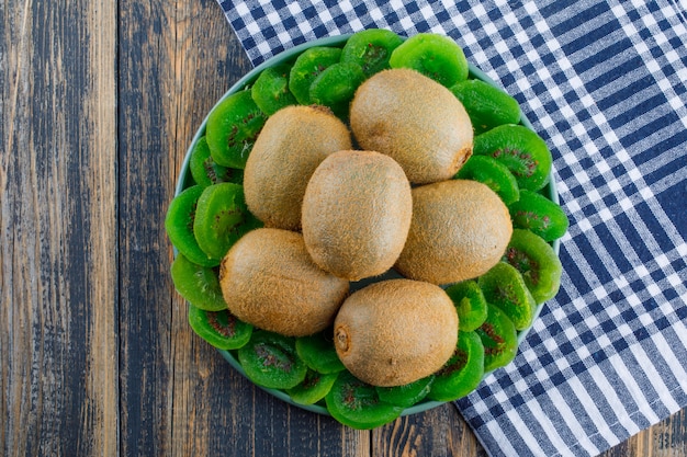 Kiwi frais avec kiwi séché dans une assiette sur fond de tissu en bois et pique-nique, pose à plat.