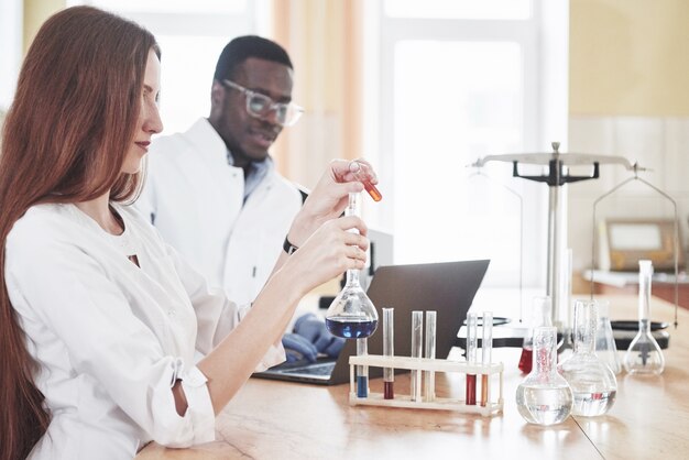 Les laboratoires de laboratoire mènent des expériences dans un laboratoire de chimie dans des flacons transparents. Formules de sortie.