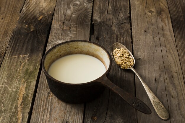 Lait dans l&#39;ancienne casserole et cuillère d&#39;avoine sur le fond en bois rustique