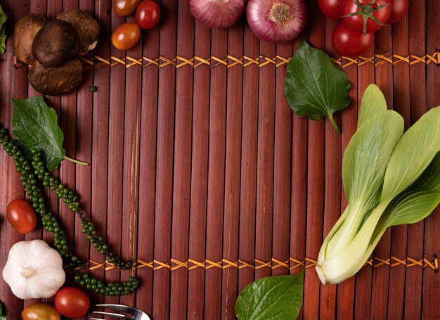 Laitue cantonaise, graines de poivre frais, ail, tomates, champignons shiitake et oignons rouges placés sur des planches de bois