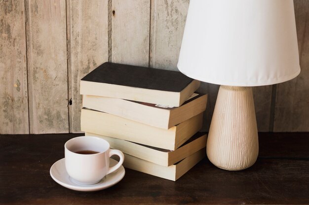 Lampe de café et pile de livres devant un mur en bois