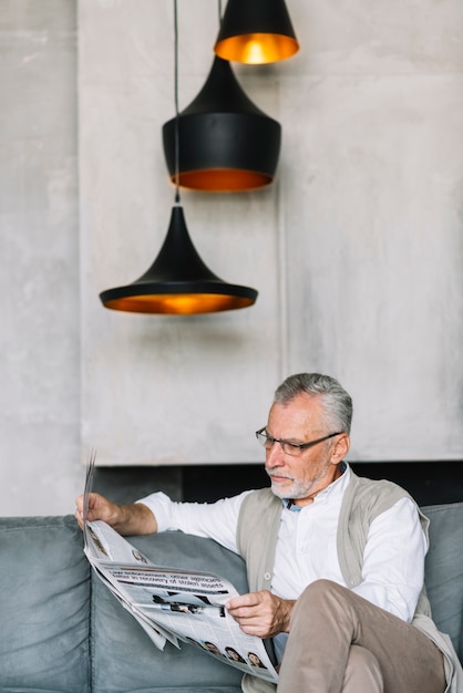 Lampes lumineuses sur l&#39;homme assis sur un canapé, lisant un journal