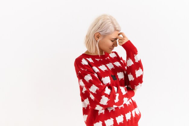 Le langage du corps. Photo d'une adolescente à la mode blonde en pull à la mode regardant vers le bas, tenant la main sur son front, essayant de se concentrer, de se souvenir de quelque chose, d'avoir une expression faciale pensive