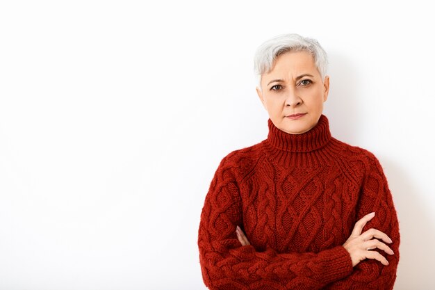 Le langage du corps. Portrait d'une femme européenne sérieuse attrayante à la retraite exprimant la méfiance ou la réticence, ayant l'air têtu, gardant les bras croisés sur sa poitrine, vêtue de pull en tricot