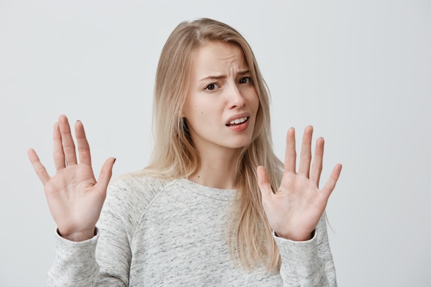 Le langage du corps. A souligné une femme portant ses cheveux blonds lâches posant contre le mur gris, gardant les mains en geste d'arrêt, essayant de se défendre comme si elle disait: