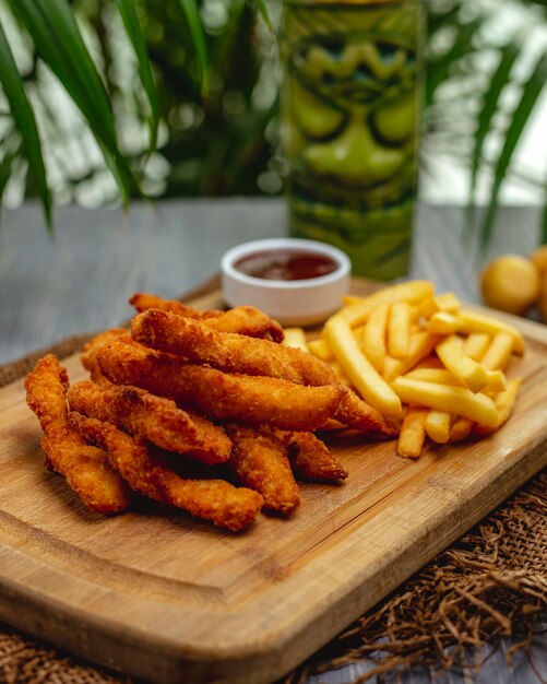 Lanières de poitrine de poulet panées frites avec du ketchup et des frites sur une planche de bois