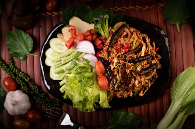 Larb de poulet dans l'assiette avec piments séchés, tomates, oignons nouveaux et laitue