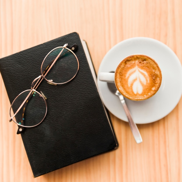 Latte de café frais à lunettes et livre sur table en bois